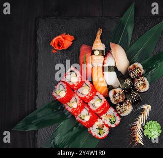 Different types of sushi are lying on green leaves on a black stone plate Stock Photo