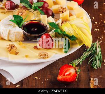 Cheese plate presenting variety of cheeses with fruits and nuts on wooden table Stock Photo