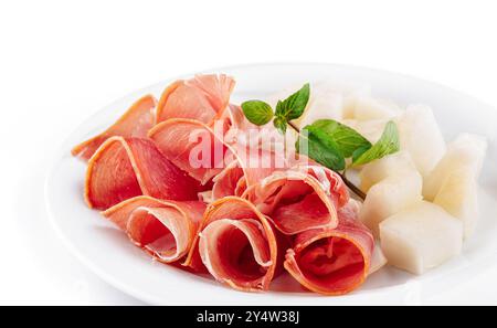 Slices of prosciutto with cantaloupe melon on a white plate garnishing with fresh mint Stock Photo