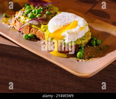 Two slices of whole grain bread with mashed avocado and poached eggs decorated with pea seeds and spices Stock Photo