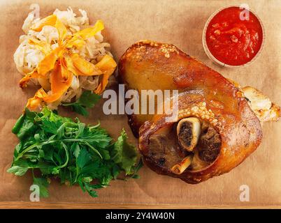 Delicious roasted pork knuckle served on wooden board with stewed cabbage, herbs and tomato sauce Stock Photo
