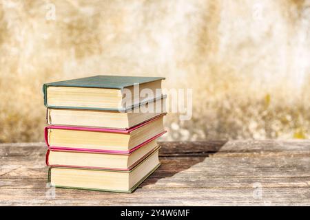 A stack of old books on an old wooden table against the background of a shabby wall plaster Stock Photo