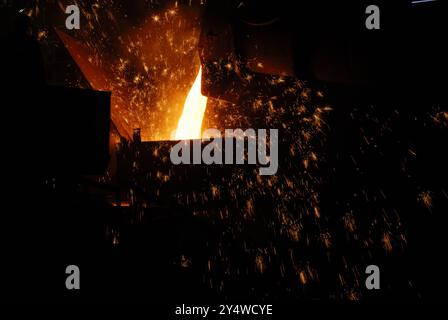 This image captures the intense moment of molten metal being poured from a furnace into a container or mold in a foundry or steel mill. The vivid oran Stock Photo