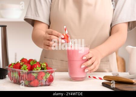 Woman with glass of tasty strawberry smoothie at table in kitchen Stock Photo