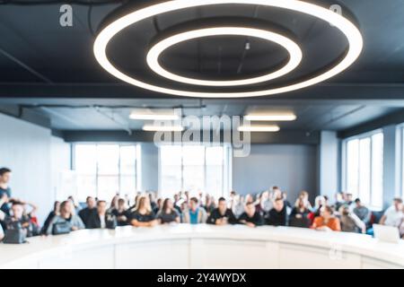 Many young people or students are sitting at a large table in a classroom or office in a blurred focus. Space for your text. High quality photo Stock Photo