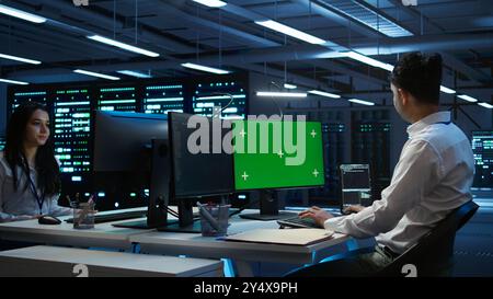 Programmer in data center managing and maintaining databases using mockup PC, ensuring data integrity and security. Expert updating server room systems using green screen computer, camera B Stock Photo