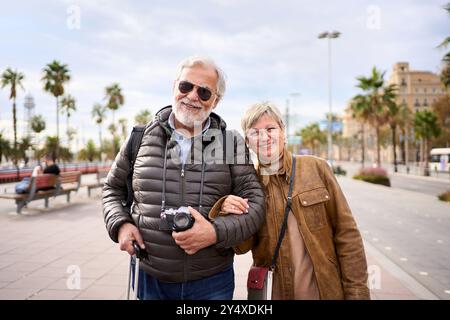 Portrait of smiling Caucasian senior tourist couple standing posing looking at camera Stock Photo