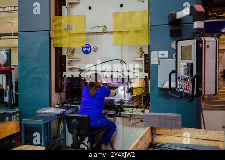 Female worker operating metal press stamping machine, close up. Stock Photo