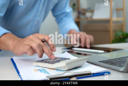 Businessman calculating taxes and finances on laptop at corporate desk, Accountant working with calculator and paperwork, Financial success, Economy c Stock Photo