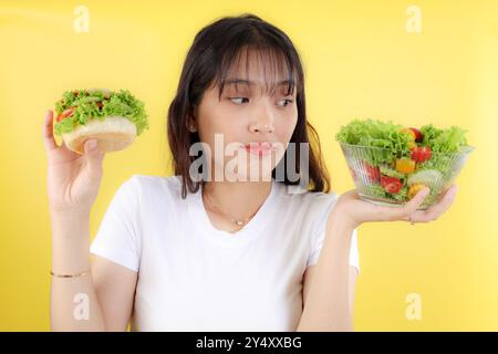 Young Asian Woman Choose Healthy Salad or Burger Junkfood with Unhappy Face. Diet Concept Stock Photo