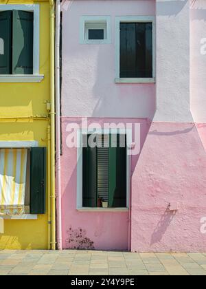 Colorful yellow and pink house walls with green shuttered windows on a bright sunny day. Stock Photo