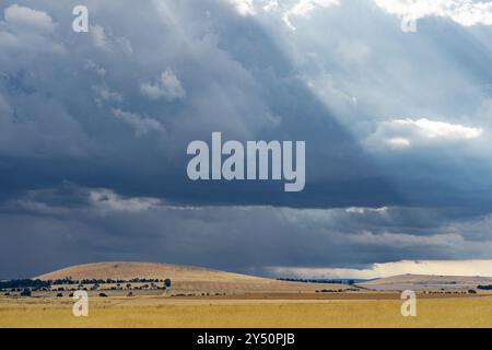 Distant view of rays of sunshine breaking through dark clouds over dry barren hill at Campbelltown in Central Victoria, Australia Stock Photo