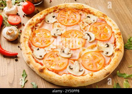 A freshly baked pizza topped with sliced tomatoes and mushrooms on a wooden table. Stock Photo