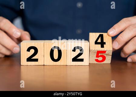 Hand flipping wooden block cube for change 2024 to 2025 for money planning and allocation concept. 2025 glowing text on the cube replaces 2024. Planni Stock Photo