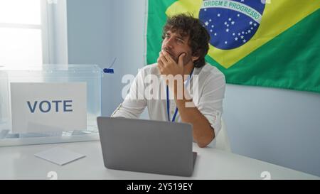 Young man in an electoral room in brazil with a voting box and flag in the background, looking thoughtful Stock Photo