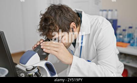 Hispanic man with beard using a microscope in a modern laboratory setting, showcasing medical research indoors. Stock Photo