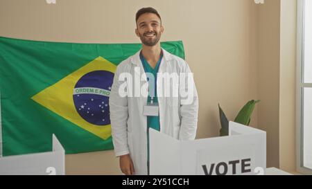 Young hispanic man at an electoral college in brazil, wearing a lab coat, smiling, with a brazilian flag in the background in an indoor setting. Stock Photo