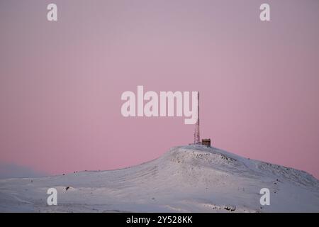Antenna mast on snow covered hill during sundown Stock Photo