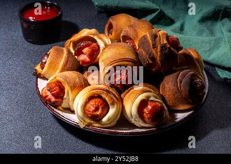 Traditional Christmas dish recipe Pigs in blankets, sausages wrapped in bacon, oven baked puff pastry hot dogs rolls with xmas tree branches, decorati Stock Photo