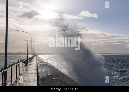 Dramatic waves crashing against a pier under a bright sky Stock Photo