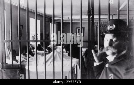 Bellevue Hospital, New York City: male patients (criminal insane?) in bed in ward, prison bars in foreground guarded by policeman. Photograph.  Date:     1885-1898 Stock Photo