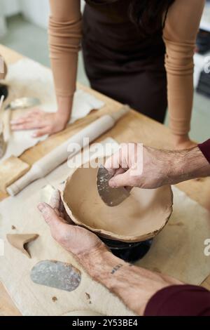 A couple shares love and creativity while shaping clay in a sunny workshop. Stock Photo