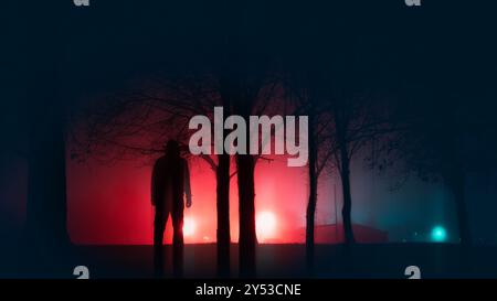 A spooky figure, silhouetted next to trees, Standing in a park. With street lights glowing on a mysterious winters night. With a blurred neon edit Stock Photo