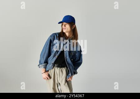 A stylish young man poses in trendy clothes and a cap against a plain backdrop. Stock Photo