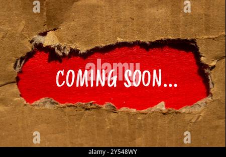 Coming soon message written on torn cardboard paper with red background. Conceptual coming soon symbol. Copy space. Stock Photo