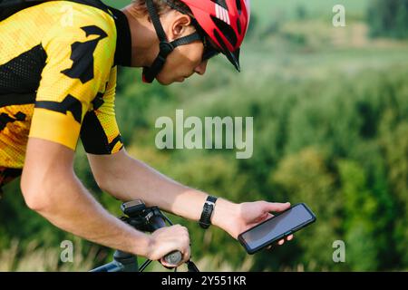 Happy male cyclist sending a text message on his mobile phone. Image of a cyclist on a mountain bike using a smartphone navigator exploring a map and Stock Photo