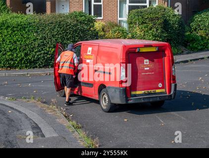 Postman in bright uniform climbing into a postal van having delivered letters to homes in Hampshire, England Stock Photo