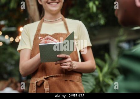 Low angle shot of pastel mint notepad in unrecognizable female hands of young waitress in eco cafe Stock Photo