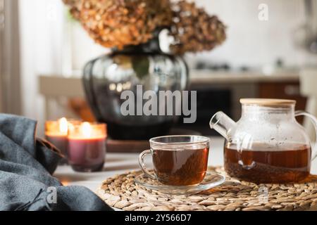 Warming autumn tea in glass cup, teapot and candles at modern kitchen. Home interior. Tea time, cozy atmosphere. Close up. Stock Photo