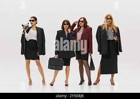 Stylish dressed women in sharp business attire and sunglasses, holding briefcases and devices against white studio background. Stock Photo