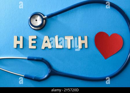 Health background with stethoscope and health message with wooden letters on blue background with red heart cutout. Top view. Stock Photo