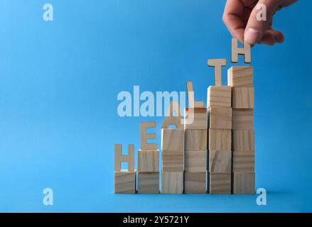 Health concept with hand placing letters forming the word health on stacks of wooden blocks on blue background. Front view Stock Photo