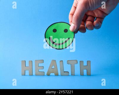 Generic health background with wooden cut out letters and hand holding green smiling emoticon isolated on blue background. Front view Stock Photo