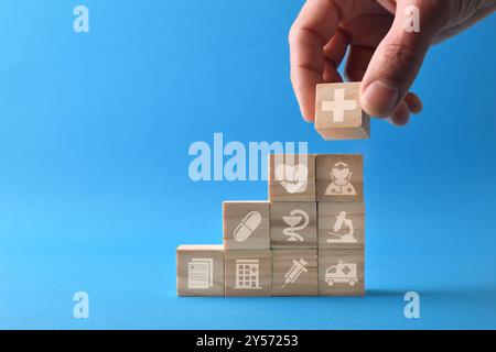 Medical care concept with hand stacking wooden cubes with symbols of different medical branches on blue table. Front view. Stock Photo