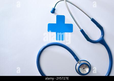 Health background with stethoscope and blue cross isolated on white table. Top view Stock Photo