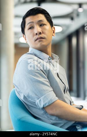 Asian man sitting in office chair, looking thoughtful and focused Stock Photo