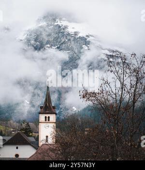 A church tower in Switzerland, surrounded by low clouds and mist. The mountains are visible in the background through the haze. Stock Photo