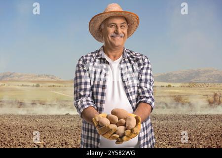 Smiling farmer holding potatoes in his hands on a field Stock Photo