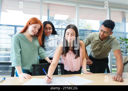 Four professionals signing documents in a bright co-working space, focused on teamwork and creative development Stock Photo