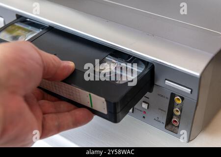 A person inserting a video cassette into a vintage video player. Stock Photo