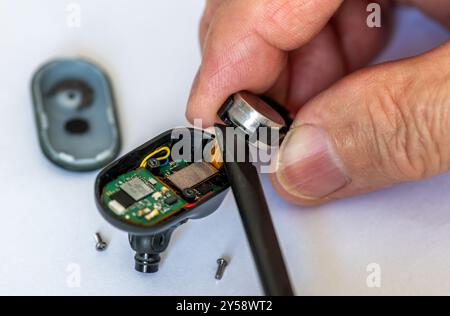 Close up of a technician using a plastic tool to replace a battery of a wireless headphone. Stock Photo