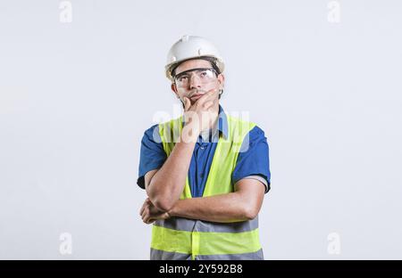 Young builder wondering looking up with hand on chin. Pensive builder man with hand on chin isolated Stock Photo