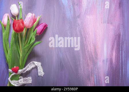Lovely bouquet of colorful tulips tied with lace ribbon and a wooden clip with red heart displayed on a wooden background with many shades of purple Stock Photo