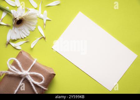 Communication theme image with a blank paper note, a torn white chrysanthemum flower and a gift box wrapped in vintage brown paper, on a yellow paper Stock Photo