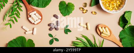 Natural vitamins, plant based supplements and green leaves on beige background, banner. Various vegan organic capsules and pills. Stock Photo