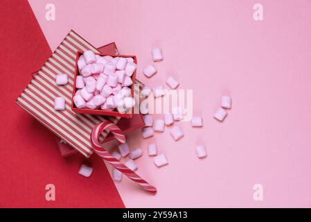 Minimalist Christmas gifts and sweets image with red presents and an open box full of pink tiny marshmallows, on a red and pink paper background Stock Photo